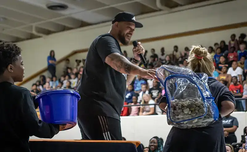 A Heroes in Waiting assembly leader engaging students in a school gym